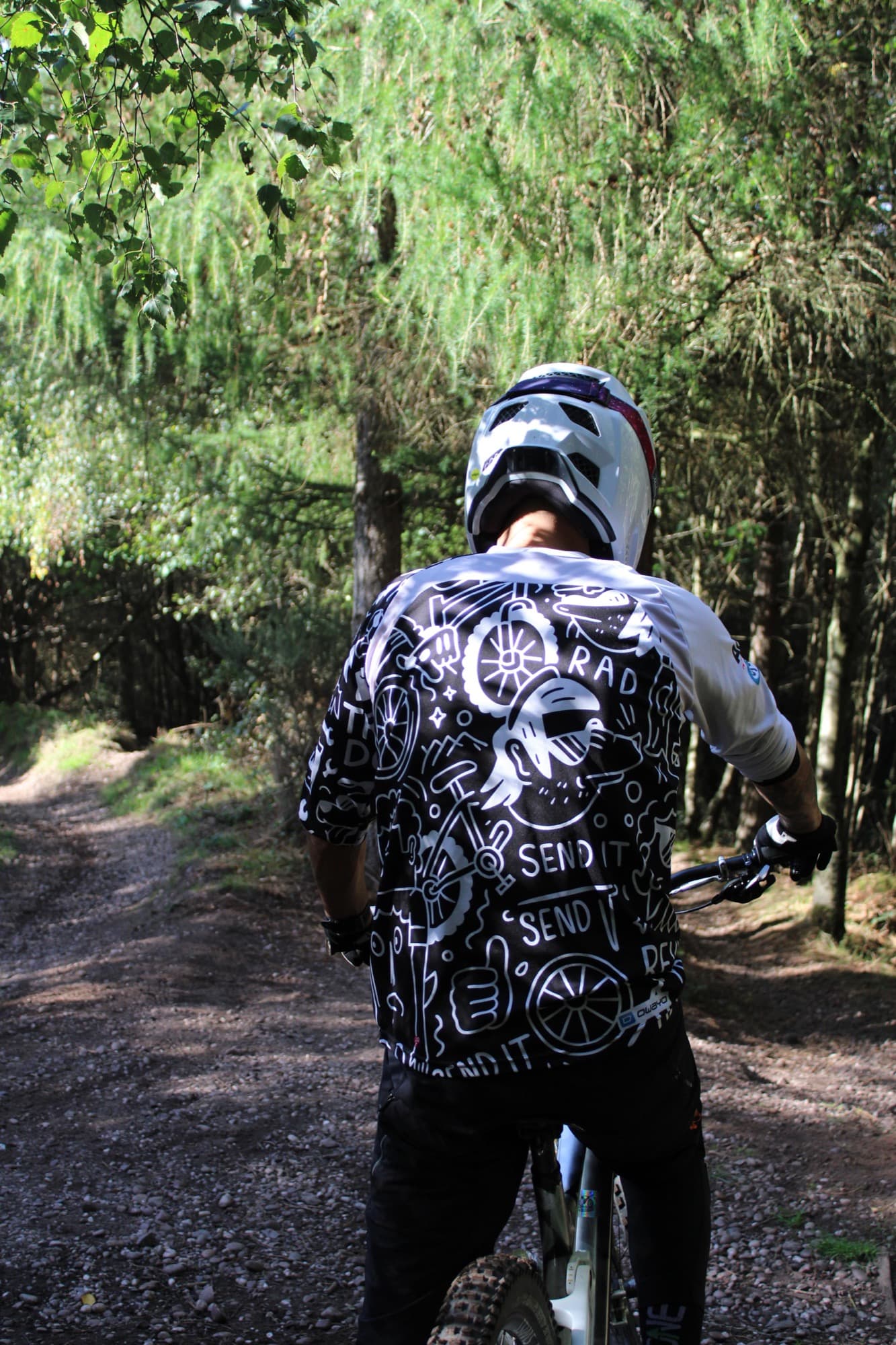 A rider in a full-face helmet on a wooded gravel track